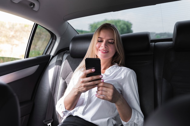 Frau, die auf dem Rücksitz des Autos simst