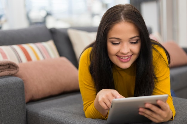 Kostenloses Foto frau, die auf dem sofa bleibt, während sie ihre tablette hält