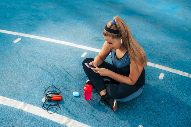 Kostenloses Foto frau, die auf dem spielplatz mit einem telefon in ihren händen sitzt