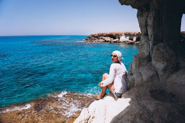 Frau, die auf die Felsenspitze durch den Ozean sitzt