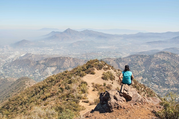 Frau, die auf einem Felsen am Rande eines Berges sitzt, während sie die Ansicht genießt