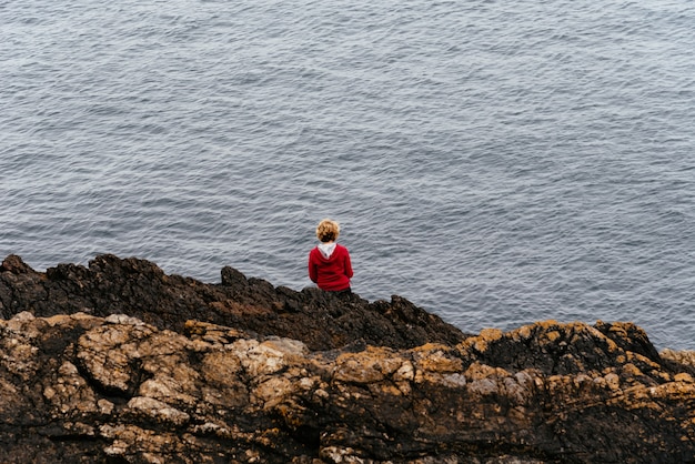 Frau, die auf einem Stein an der Küste eines Meeres sitzt