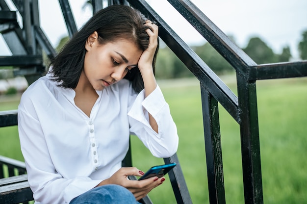 Frau, die auf einer Leiter betrachtet ein intelligentes Telefon und hat Druck sitzt