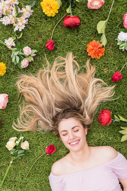 Frau, die auf Gras mit verschiedenen Blumen liegt