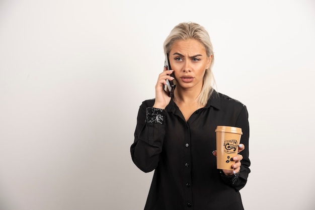 Frau, die auf handy spricht und eine tasse kaffee hält. hochwertiges foto