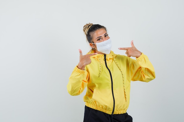 Frau, die auf ihre Maske in der Vorderansicht des Sportanzugs zeigt.