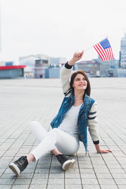 Frau, die auf quadrat sitzt und in der hand amerikanische flagge wellenartig bewegt