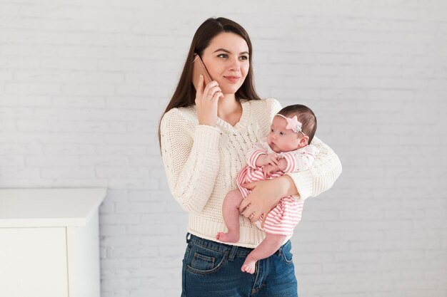 Frau, die auf Smartphone spricht und kleines Baby hält