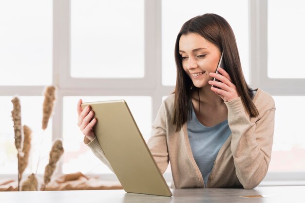 Frau, die auf Smartphone spricht und Tablette hält