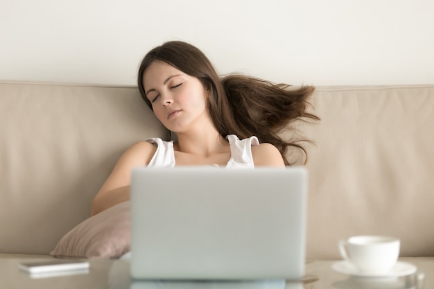 Frau, die auf Sofa vor Laptop einschläft