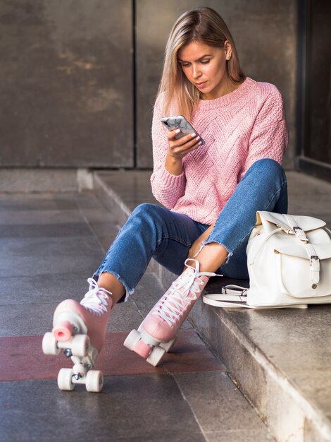 Frau, die auf Treppe mit Rollschuhen sitzt und Smartphone betrachtet