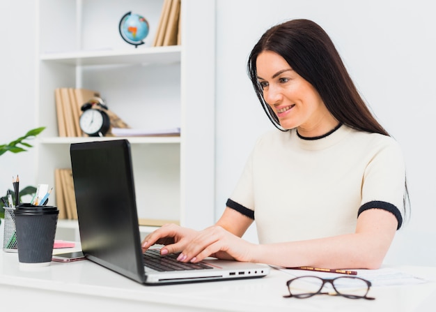 Frau, die bei Tisch auf Laptoptastatur schreibt