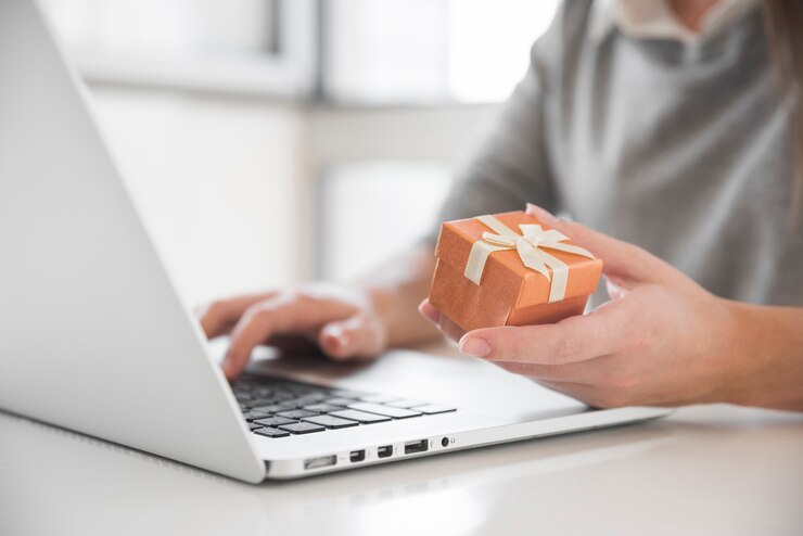 Kostenlose Foto frau, die bei tisch mit laptop und geschenkbox sitzt