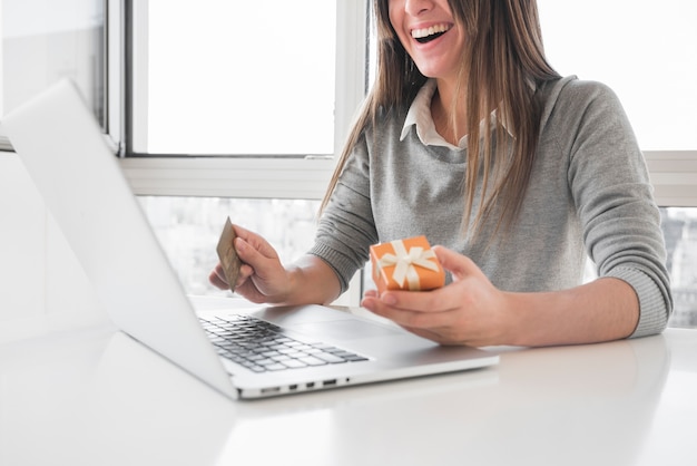 Frau, die bei Tisch mit Laptop und Kreditkarte sitzt