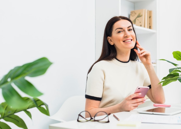 Kostenloses Foto frau, die bei tisch mit smartphone im büro sitzt