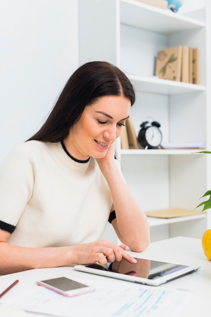 Frau, die bei Tisch Tablette im Büro verwendet