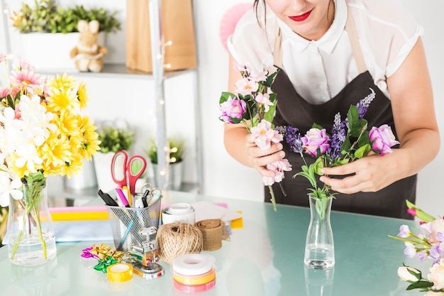 Kostenloses Foto frau, die blumen in vase auf glasschreibtisch setzt