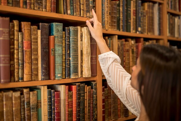 Frau, die Buch vom Bücherregal in der Bibliothek wählt