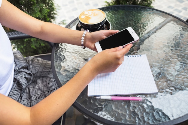 Frau, die Café am im Freien unter Verwendung des Mobiltelefons sitzt