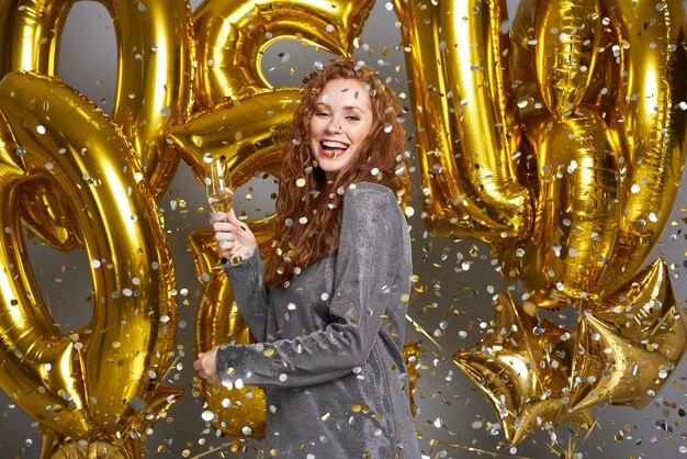 Frau, die Champagner unter der Dusche von Konfetti trinkt