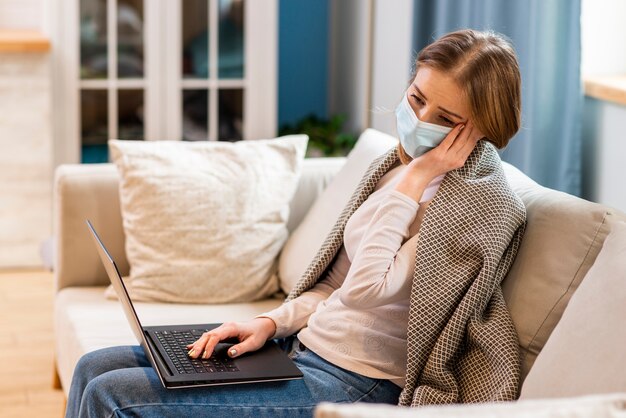 Frau, die chirurgische Gesichtsmaske trägt und auf Couch sitzt