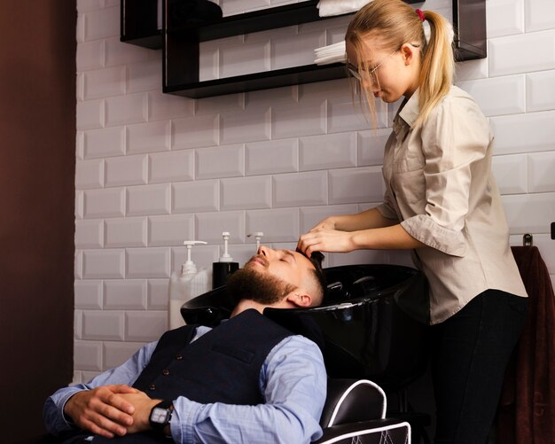 Frau, die das Haar eines Mannes am Friseursalon wäscht