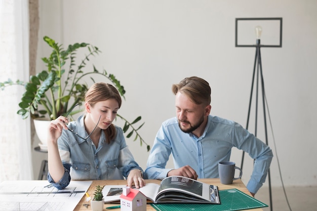 Kostenloses Foto frau, die das schauspiel betrachtet innenkatalog mit ihrem männlichen mitarbeiter im büro hält