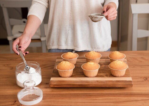 Frau, die das Sieb sich vorbereitet, Muffins mit Zucker zu besprühen hält