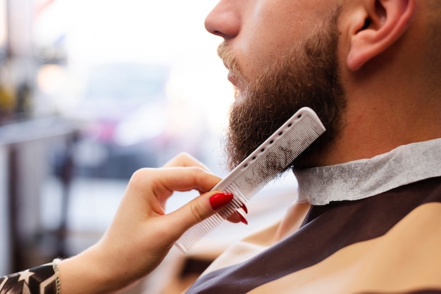 Frau, die den Bart eines Mannes an einer Berufsfriseursalonnahaufnahme pflegt