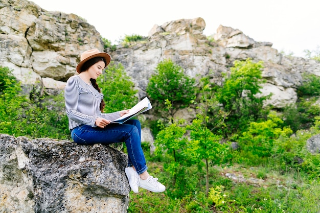 Frau, die die Karte sitzt auf einem Felsen betrachtet