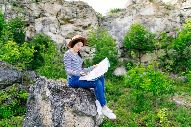 Frau, die die Karte sitzt auf einem Felsen betrachtet