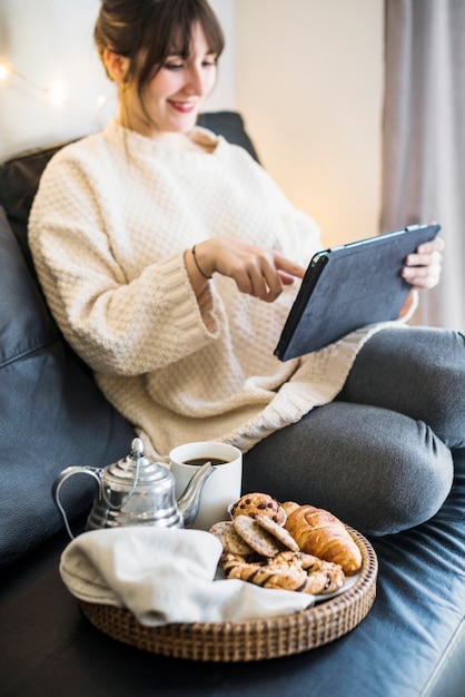 Frau, die digitale Tablette mit Frühstück auf Sofa verwendet