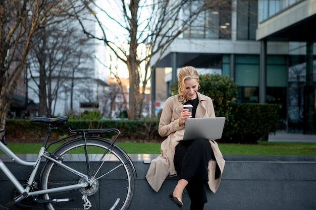 Frau, die draußen an ihrem Laptop arbeitet und Kaffee trinkt