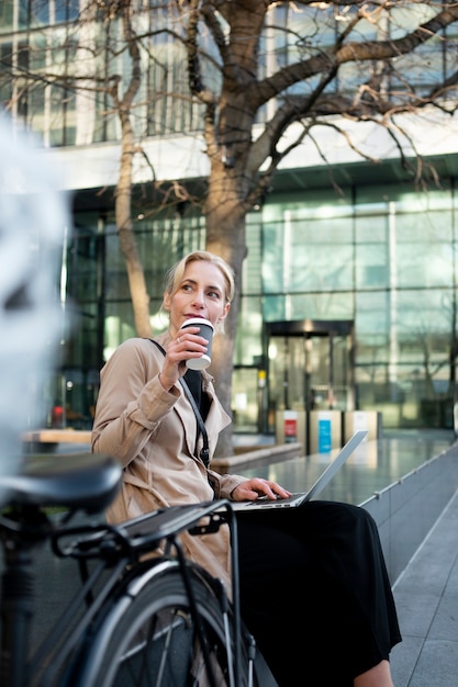 Frau, die draußen an ihrem Laptop arbeitet und Kaffee trinkt