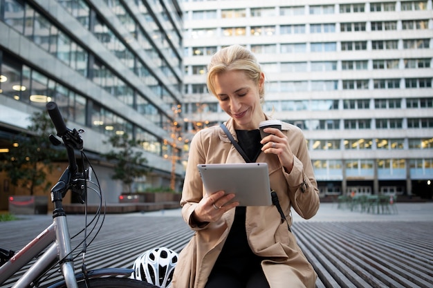 Frau, die draußen an ihrem Tablet arbeitet und Kaffee trinkt