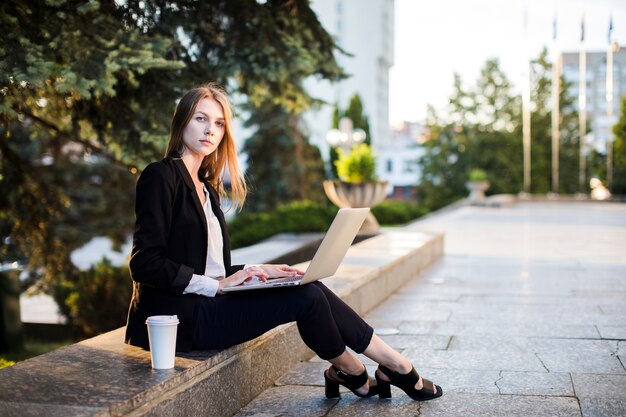 Frau, die draußen mit Laptop sitzt