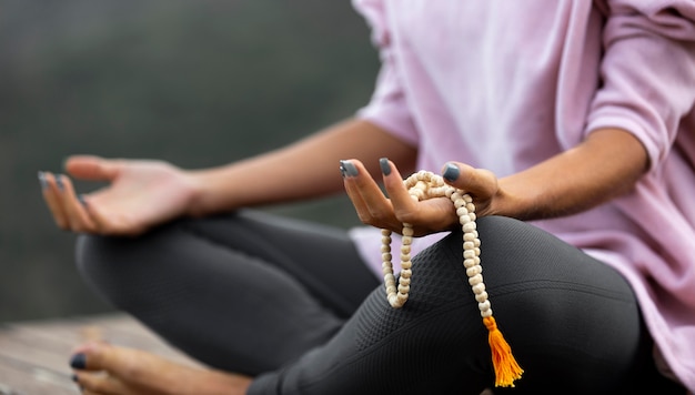 Frau, die draußen Yoga macht und Rosenkranz hält