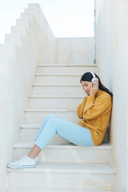 Frau, die durch hörende Musik mit den Kopfhörern sitzen auf Schritten sich entspannt