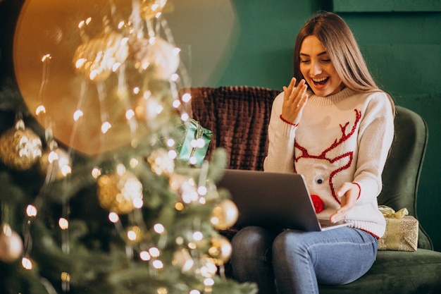 Frau, die durch Weihnachtsbaum sitzt und Online-Verkäufe kauft