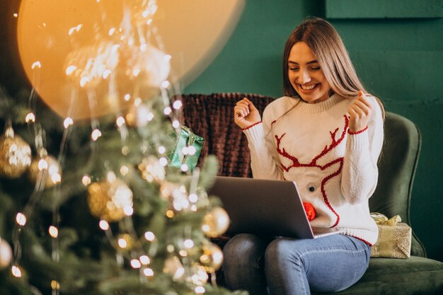 Frau, die durch Weihnachtsbaum sitzt und Online-Verkäufe kauft