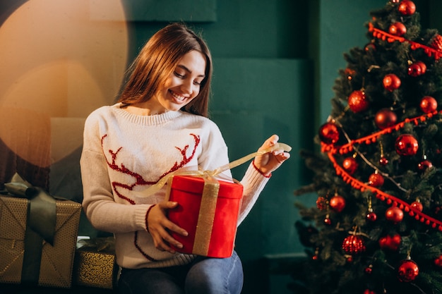 Frau, die durch Weihnachtsbaum sitzt und Weihnachtsgeschenk auspackt