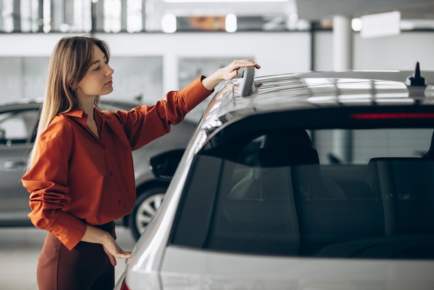 Frau, die ein auto in einem autosalon wählt