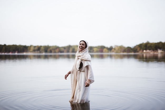 Frau, die ein biblisches Gewand trägt und lacht, während sie im Wasser steht
