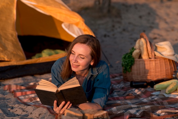 Frau, die ein Buch auf Picknickdecke liest