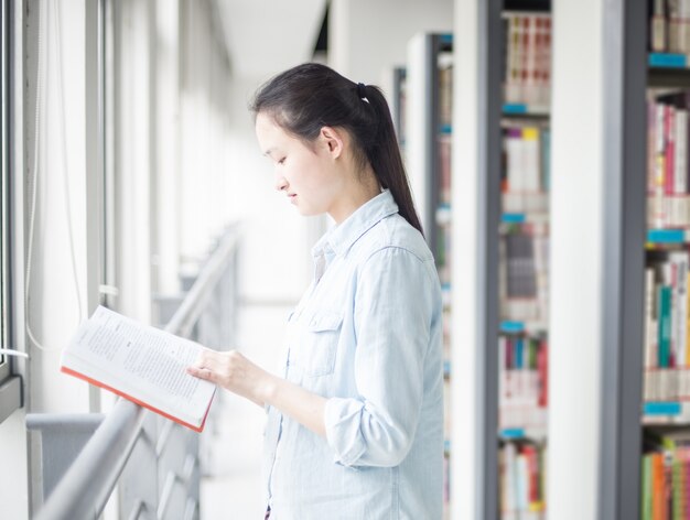 Frau, die ein Buch in der Nähe von einem Fenster lesen