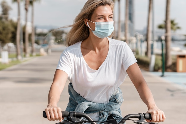 Kostenloses Foto frau, die ein fahrrad reitet, während sie eine medizinische maske trägt