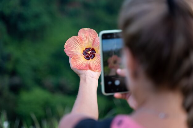 Frau, die ein Foto mit ihrem Handy einer Blume macht, die sie in ihrer Hand hält