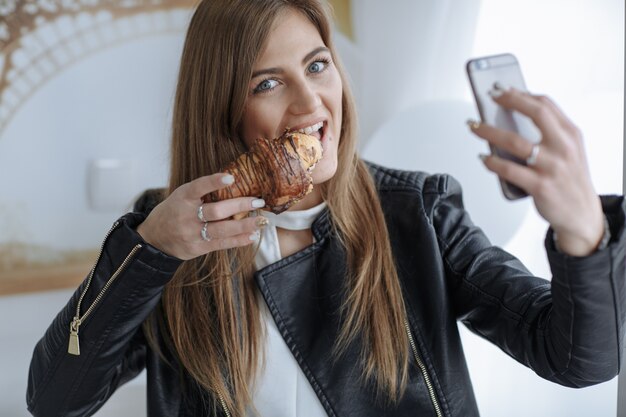 Frau, die ein Foto mit ihrem Handy zu machen, während ein Croissant essen