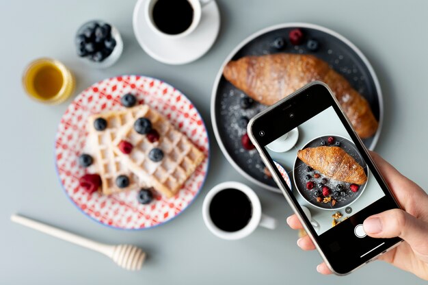 Frau, die ein Foto von Croissants mit Früchten macht