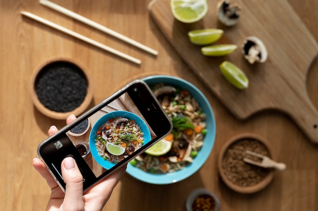 Kostenloses Foto frau, die ein foto von einer schüssel ramen und geschnittener zitrone macht